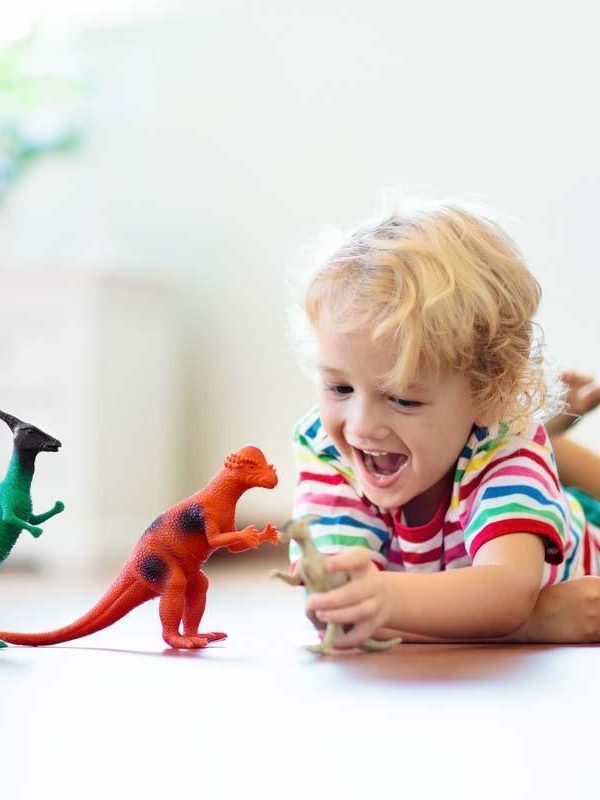 Child playing with colorful toy dinosaurs. Educational toys for kids. Little boy learning fossils and reptiles. Children play with dinosaur toys. Evolution and paleontology game for young kid.