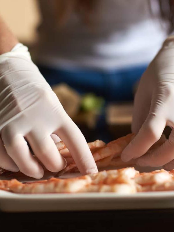 Close-up view of woman's hands in gloves are preparing shrimp for rolling sushi in restaurant